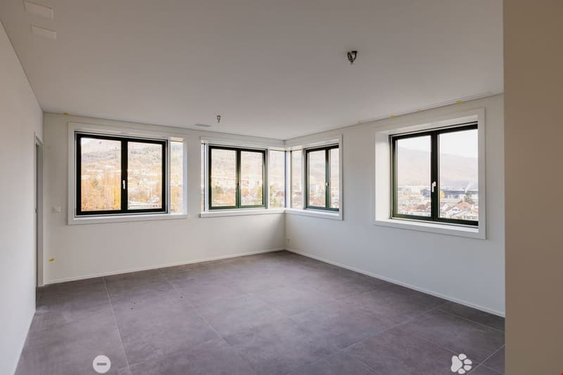 Empty room, 3 windows, white walls, gray floor, outside view of city