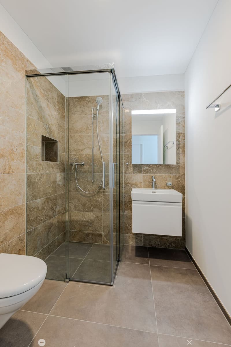 A modern bathroom with a glass shower, white toilet, white sink, and tiled walls.