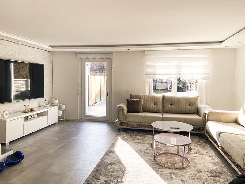 modern living room with white walls, gray floor, two couches, coffee table, TV, white entertainment center, glass door