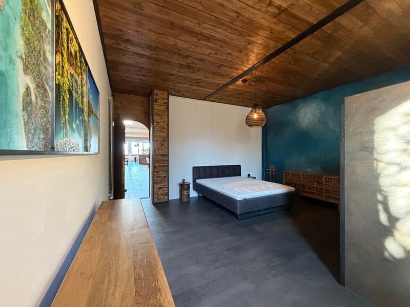 bedroom with wooden ceiling, bed, wooden bench, wooden floor, blue wall, white wall, wooden cabinet, lamp
