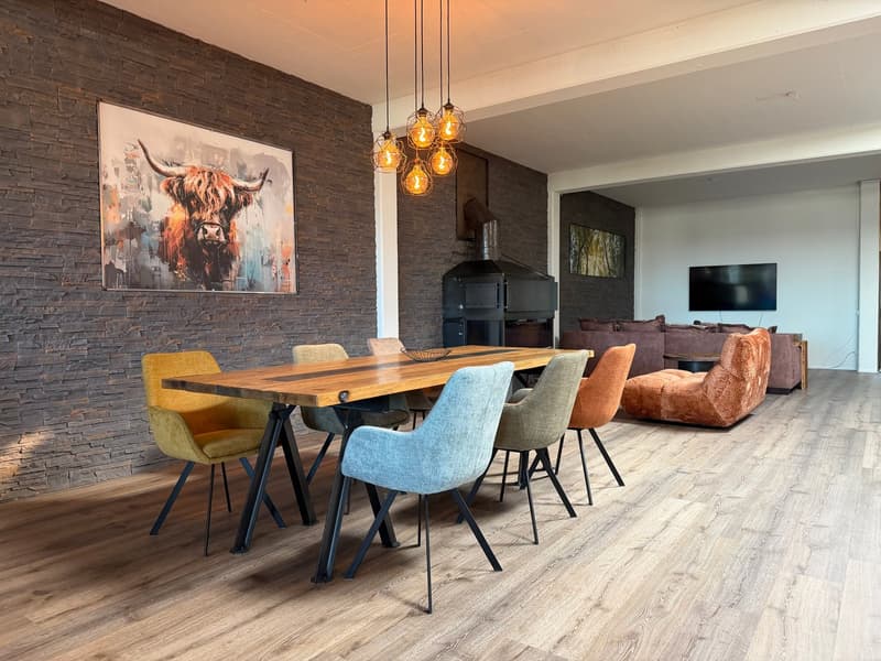 Dining room with wooden table, 6 chairs, brick wall, fireplace, TV, couch, artwork
