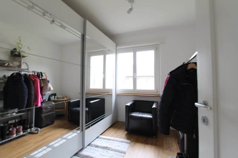 Spacious bedroom with large windows, hardwood flooring, built-in closet system, and a comfortable armchair