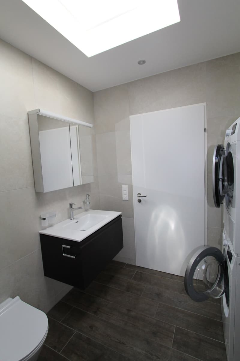 Modern bathroom with a vanity sink, mirror cabinet, and a washing machine.