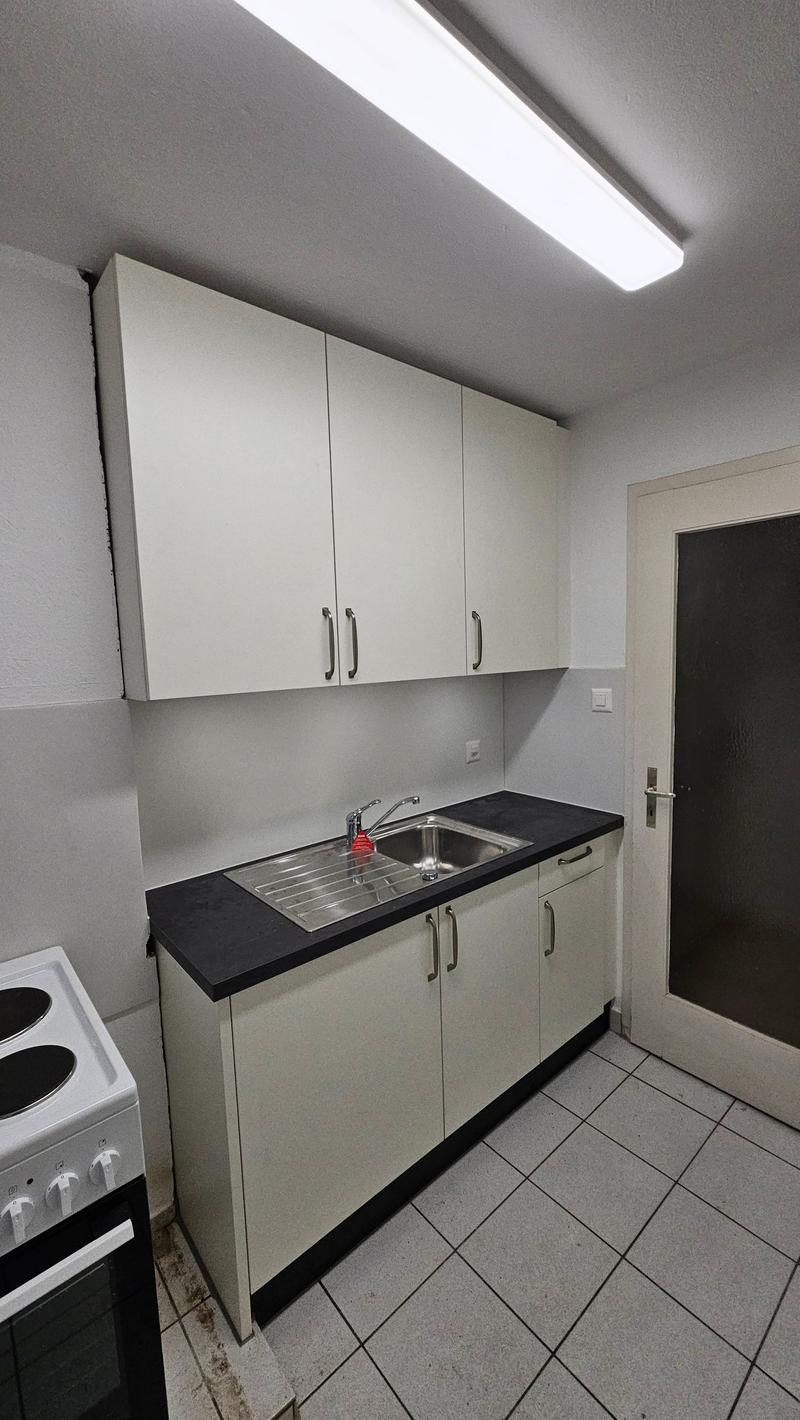 tiled floor, white kitchen cabinets, gas stove, black countertop, stainless steel sink