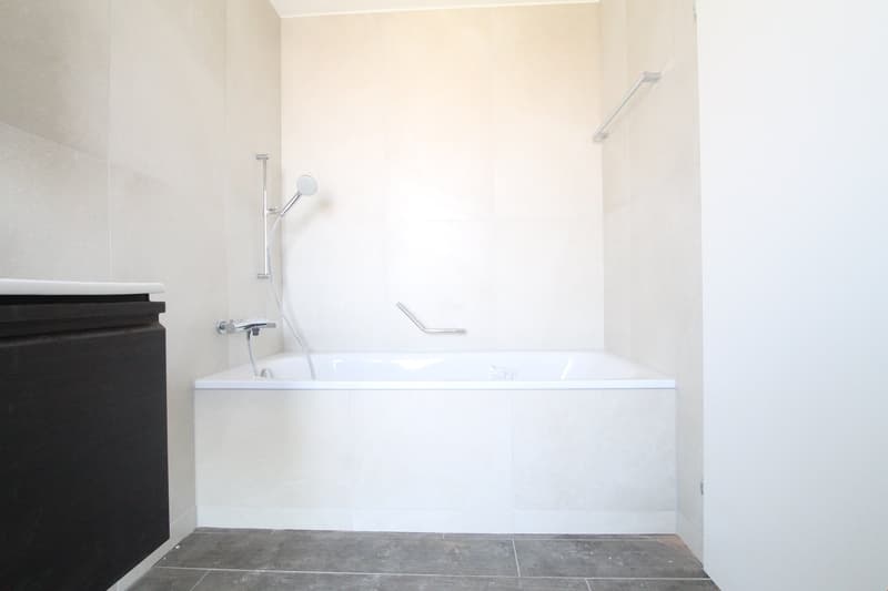 modern bathroom, white bathtub, white tiles, shower head, black cabinet