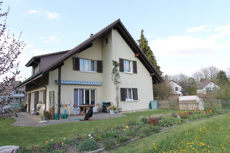 2 story house, beige exterior, brown roof, large windows, garden, patio, dog