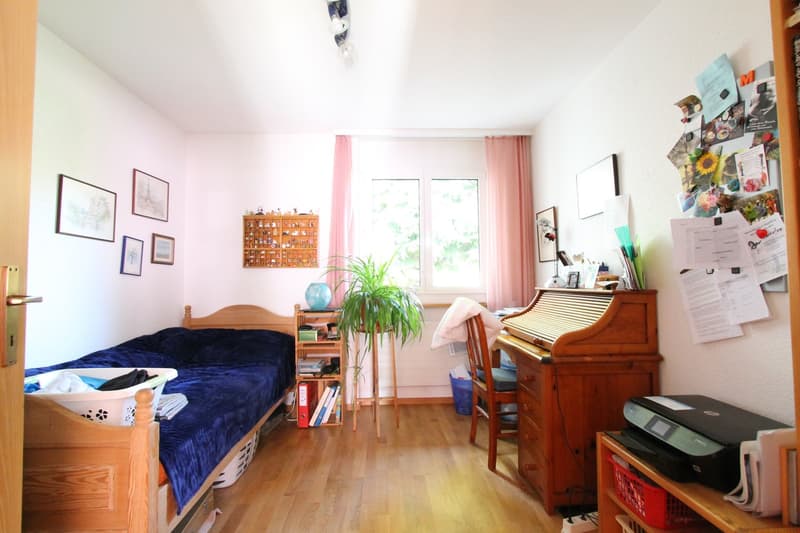 bedroom with bed, wooden desk, printer, plant, books, wooden floor