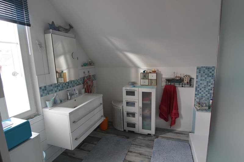 Bathroom with white sink, white cabinet, blue tiles, window, red towel, blue rug, wooden floor