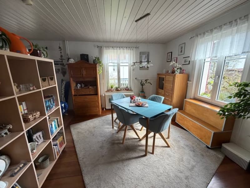 Dining room with a blue table and chairs, a wooden cabinet, a shelf with books, a radiator, and a white rug.