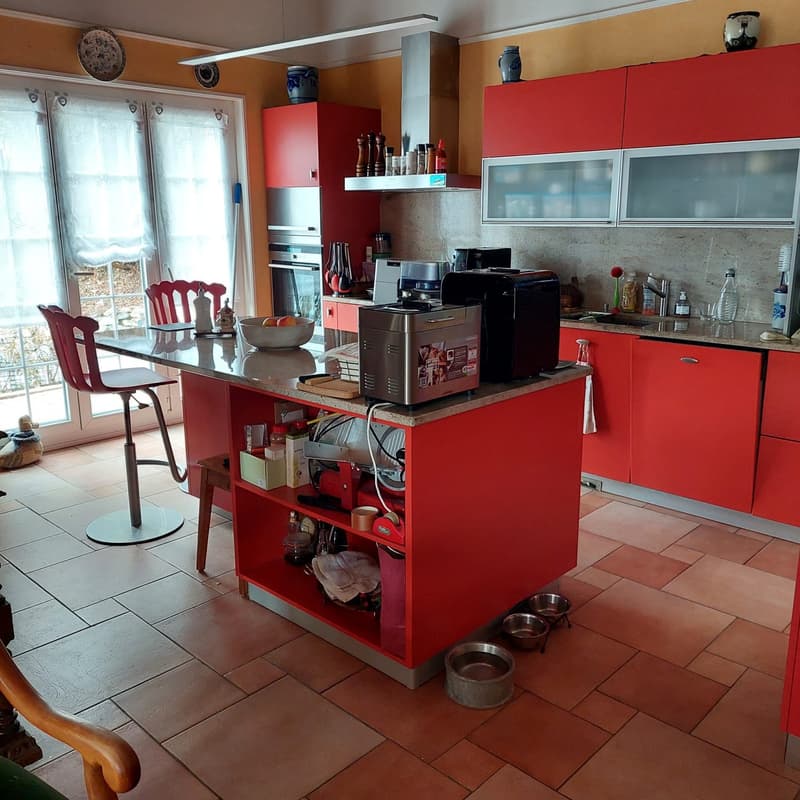 Central kitchen island with a countertop, a variety of appliances, red cabinets, a red chair, a glass door.