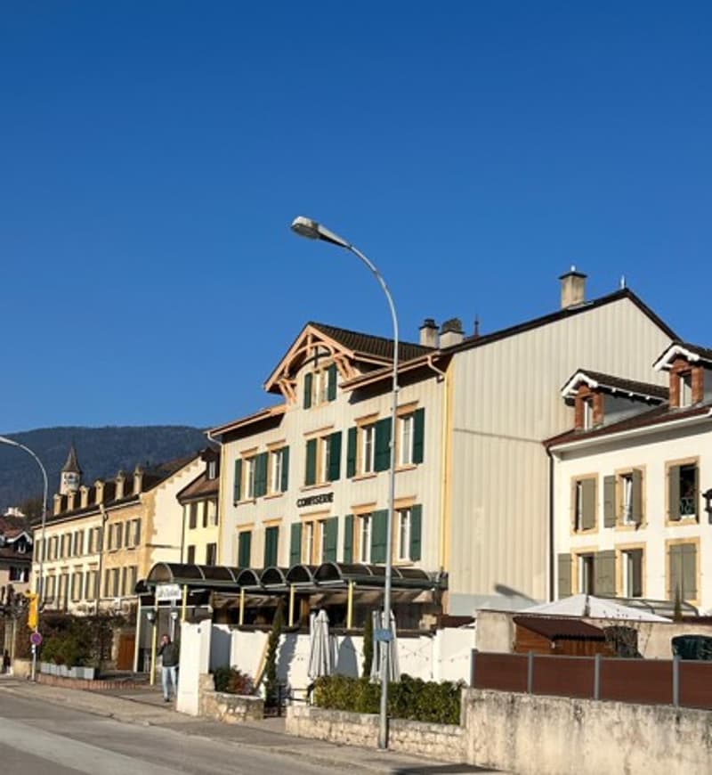 Building with yellow facade, windows with green shutters, streetlight, outdoor seating