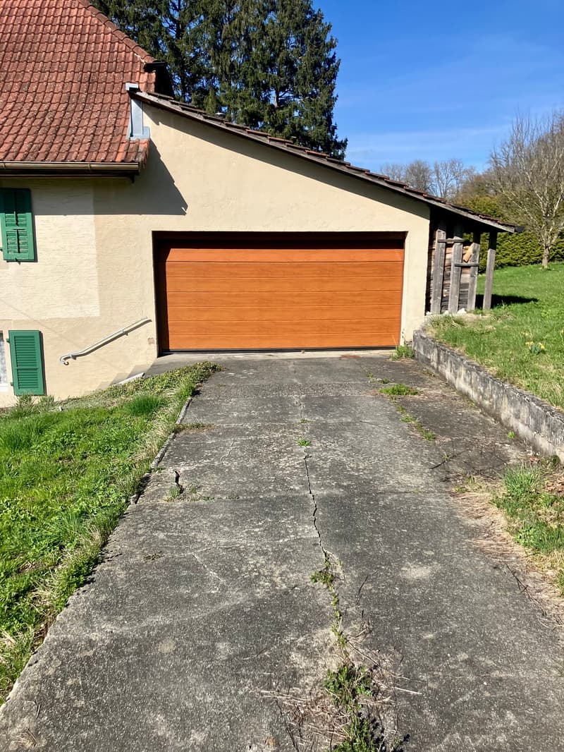 House with brown wooden garage door, red roof, green shutters, concrete driveway