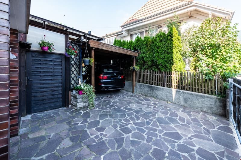 car in garage, gravel driveway, black metal gate, wooden fence, greenery