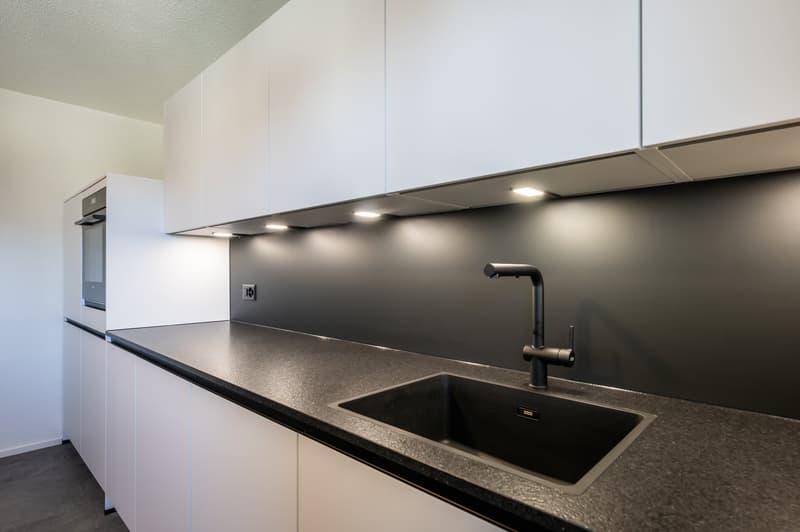 modern kitchen with white cabinets, black countertops, stainless steel sink, black faucet, built-in oven, under-cabinet lighting