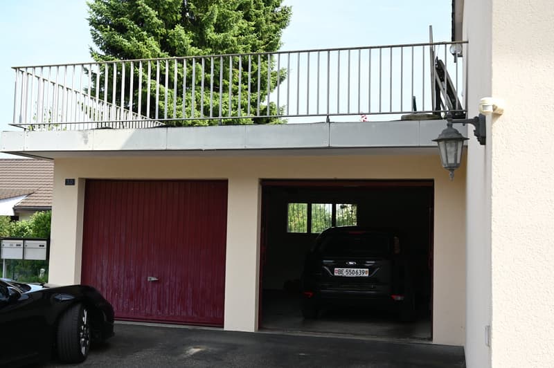 Metal railing, two garage doors, a black car parked inside, and a white box near the left door