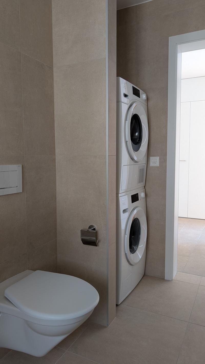 beige tiled walls, toilet, towel rack, washer and dryer, outlet, cabinet
