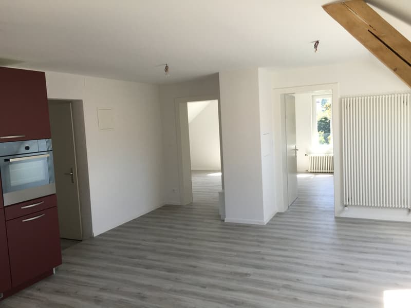empty room, wooden floors, white walls, kitchen appliances, radiators, open doorways, slanted ceilings