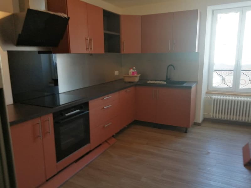 Modern kitchen with wooden floor, black countertops, wooden cabinets, built-in oven, sink with faucet, window with view