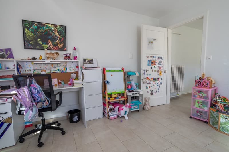 A room with a desk, chair, shelves, toys, and a refrigerator.