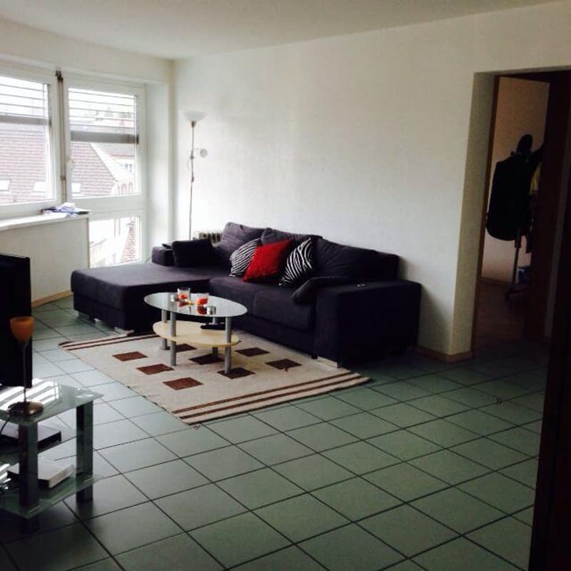 Living room with a couch, coffee table, rug, and a window with blinds