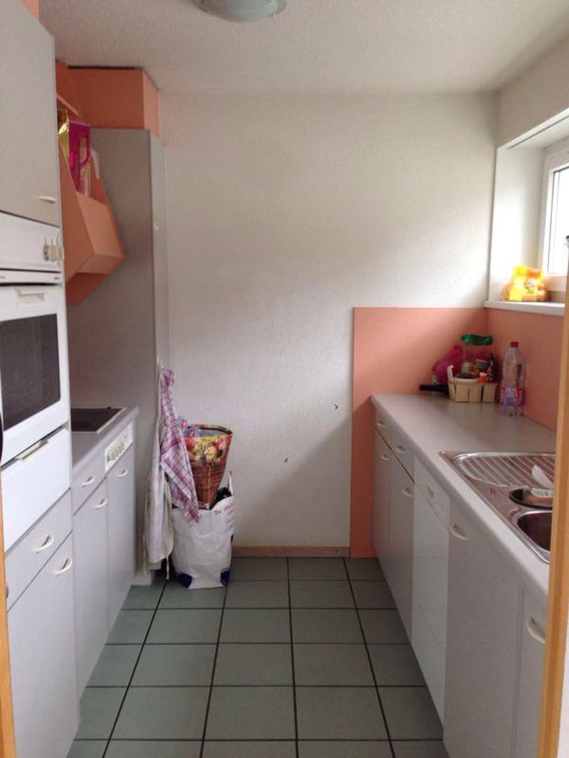 small kitchen with white cabinets, tiled floor, white oven, sink, countertop, trash bin, basket, and a window
