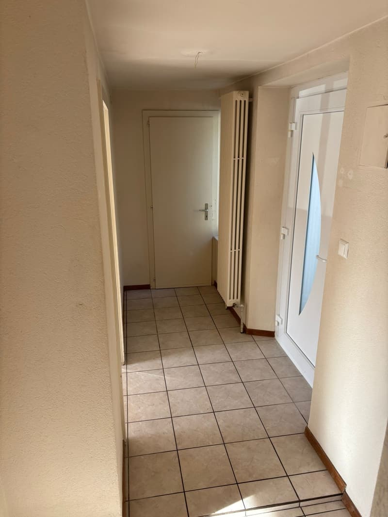 Empty corridor with tiled floor, two white doors, and a radiator.