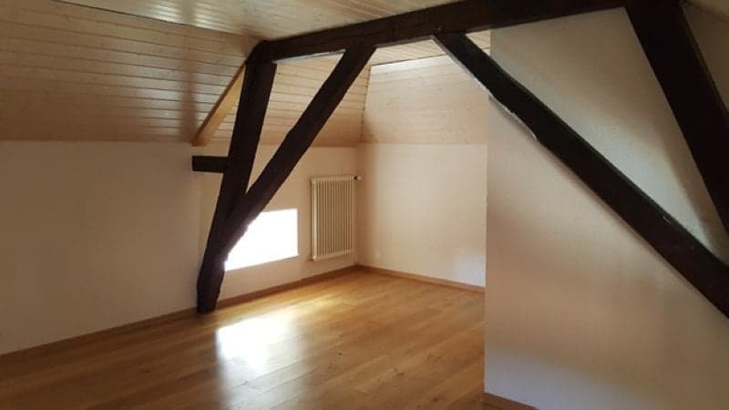 Empty room with wooden floor, white walls, wooden beams, and a window.