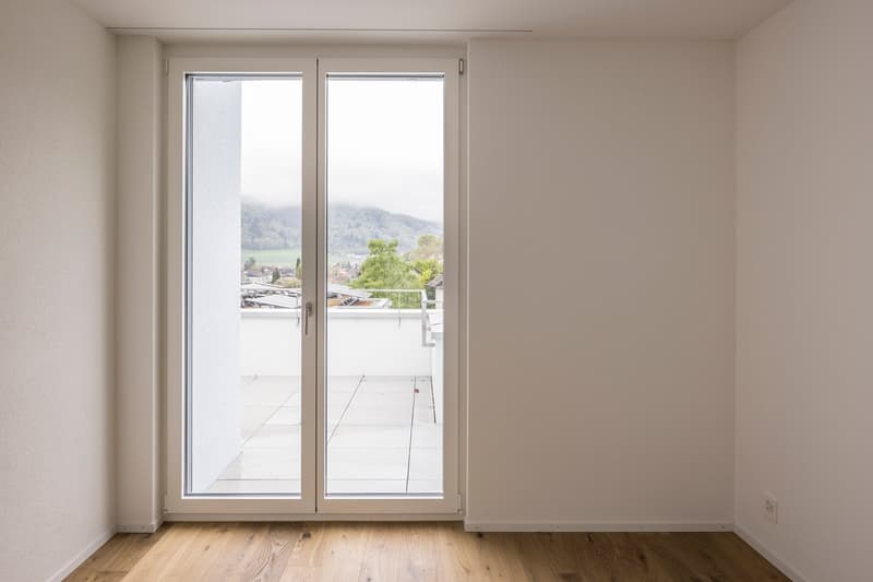 empty room, large glass sliding doors, wooden floor, white walls, balcony with view