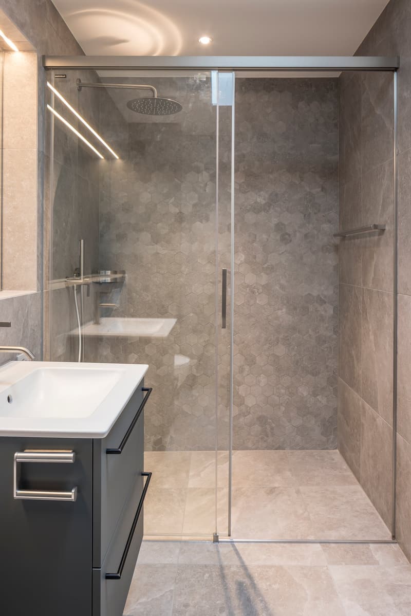 modern bathroom with glass shower enclosure, hexagonal tiles, white sink, gray vanity, silver fixtures