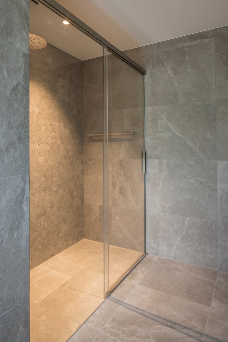 shower room with glass door, tiled floor, hexagonal tiles on wall, silver shower head