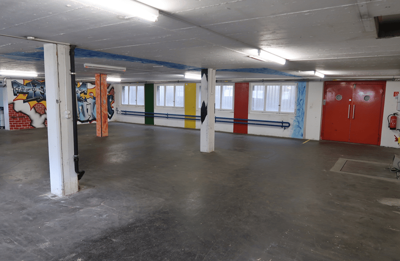 Empty parking space, fluorescent lighting, graffiti on the wall, red and yellow doors, black pipe