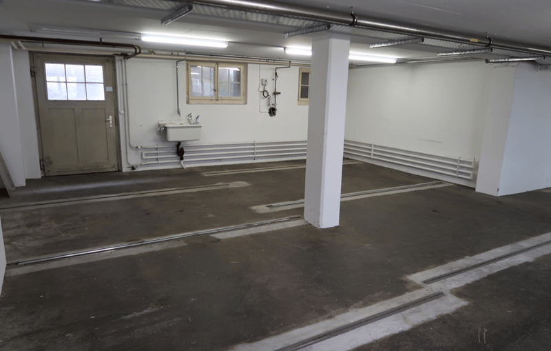 Empty garage with white walls, grey concrete floor, two windows, and a white sink