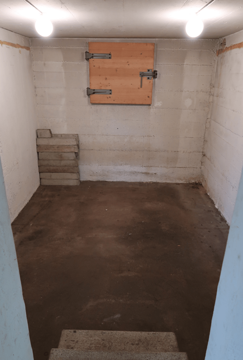 Concrete floor, stack of cement blocks, wooden entrance door, concrete wall