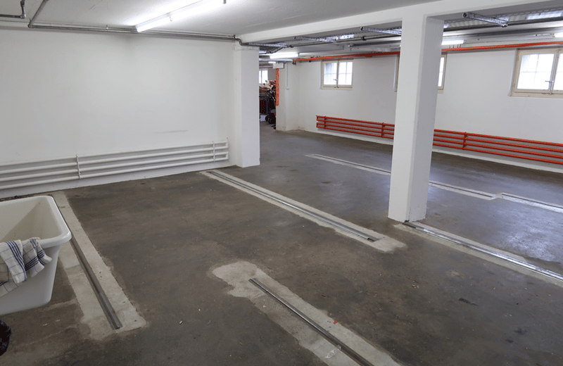 empty concrete floor, white walls, piped white radiators on the wall, and metal railings on the wall
