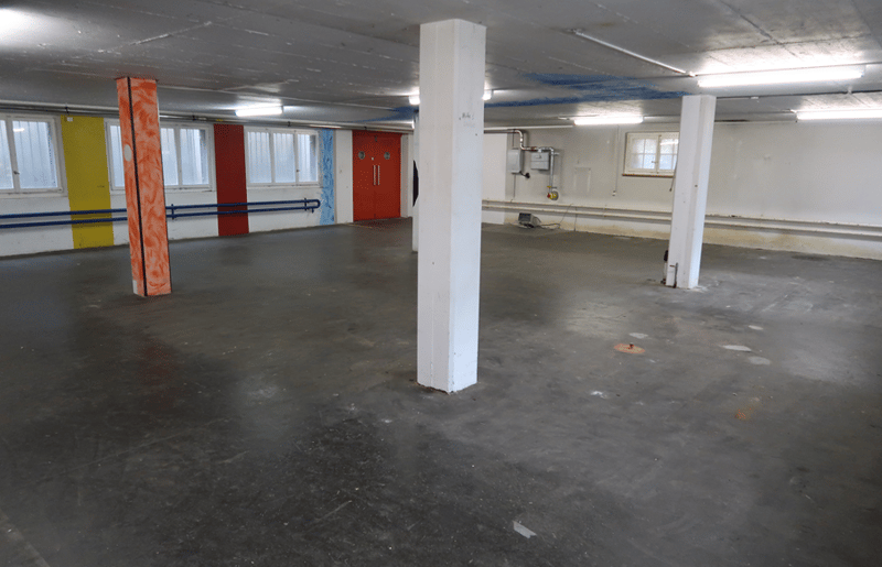 Empty parking lot, white walls, two doors, and multiple windows.