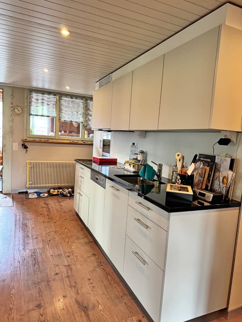 modern kitchen with white cabinets, black countertops, wooden floor, dishwasher, washing machine, sink, faucet, window, radiator