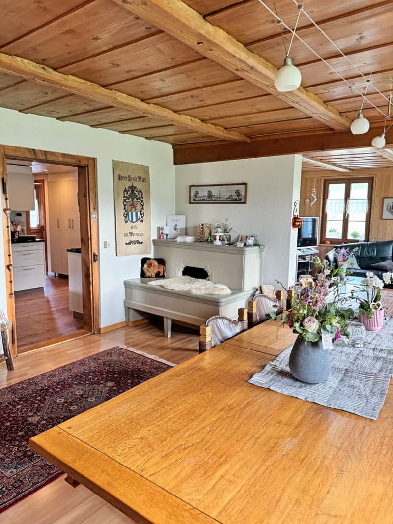 Dining room with wooden ceiling, dining table, chairs, rug, fireplace, flower vase, TV, couch, kitchen