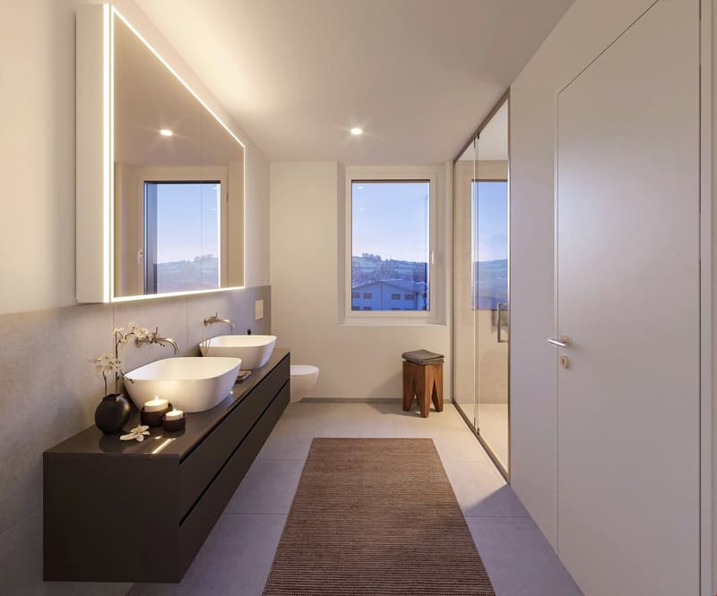 Spacious bathroom with double vanity sinks, large mirror with integrated lighting, glass shower enclosure, and a view of the surrounding landscape through the window.