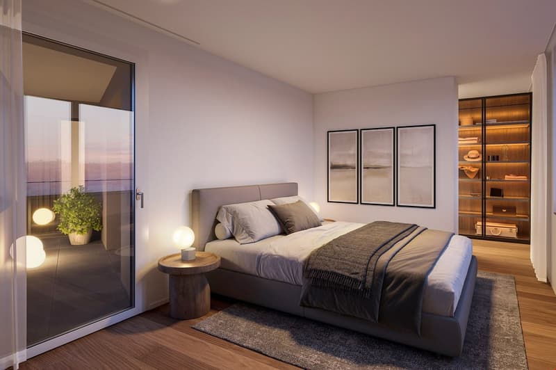 Spacious bedroom with large windows providing a scenic view, grey upholstered bed frame, bedside tables, framed artwork on the wall, and a built-in shelving unit.