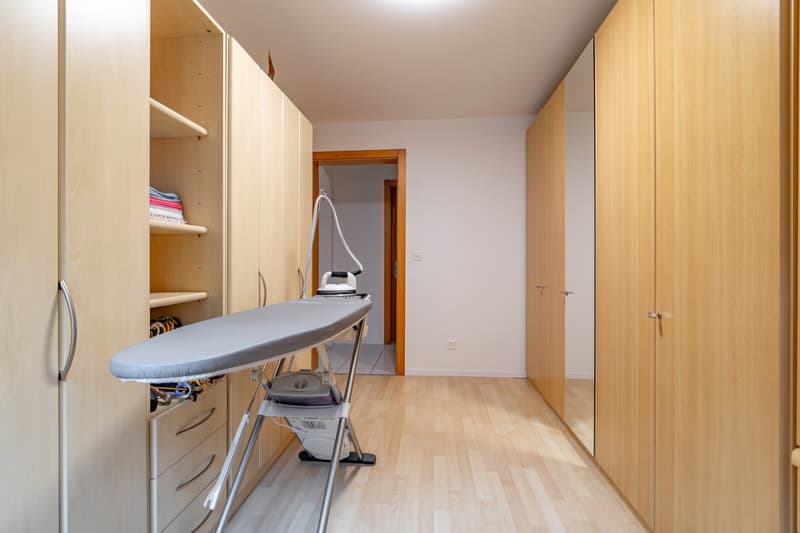 Closet with shelves, iron and ironing board, wardrobes, drawers, wooden floor, white walls