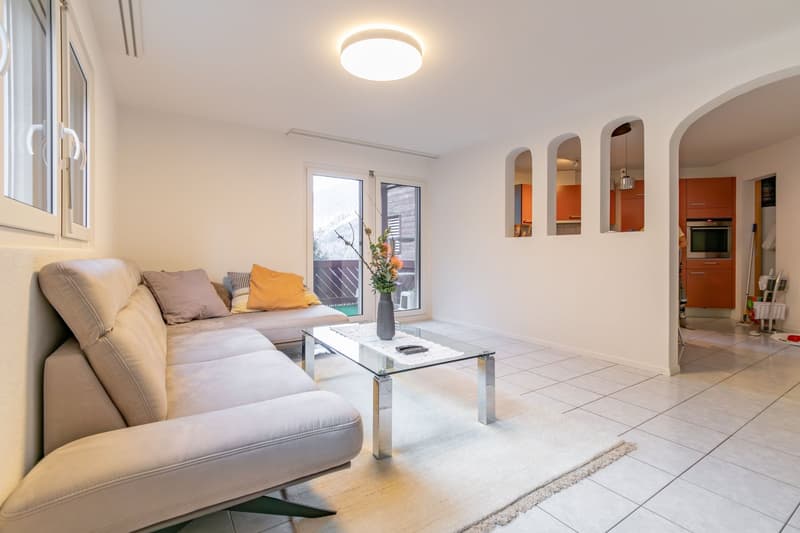 modern living room with a large sofa, a glass coffee table, white tile flooring, and large windows leading to a balcony