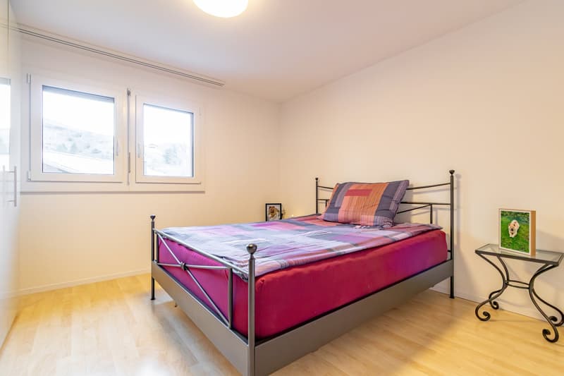a bedroom with a bed, nightstand, picture frame, windows, and wooden floor