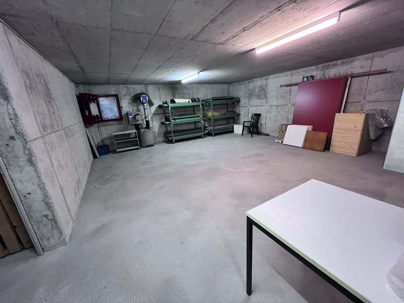 Concrete walls and floor, storage shelves, various boxes and furniture items, a table, and a dimly lit interior.