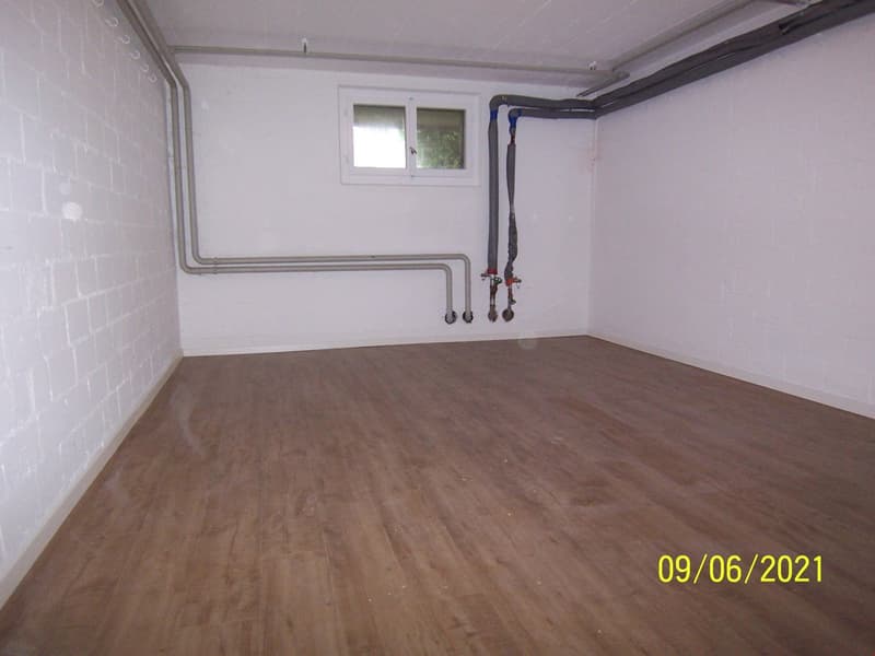 Empty room with wooden floor, white walls, small window, pipes on the wall