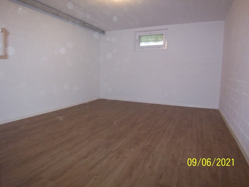 Empty room with wooden floor, white walls, small window, and a pipe on the ceiling.