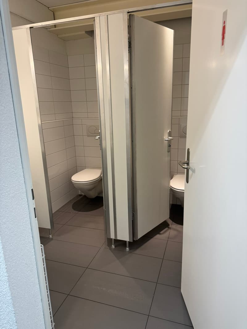Two separate toilet stalls with tiled walls and floors, metal stall dividers