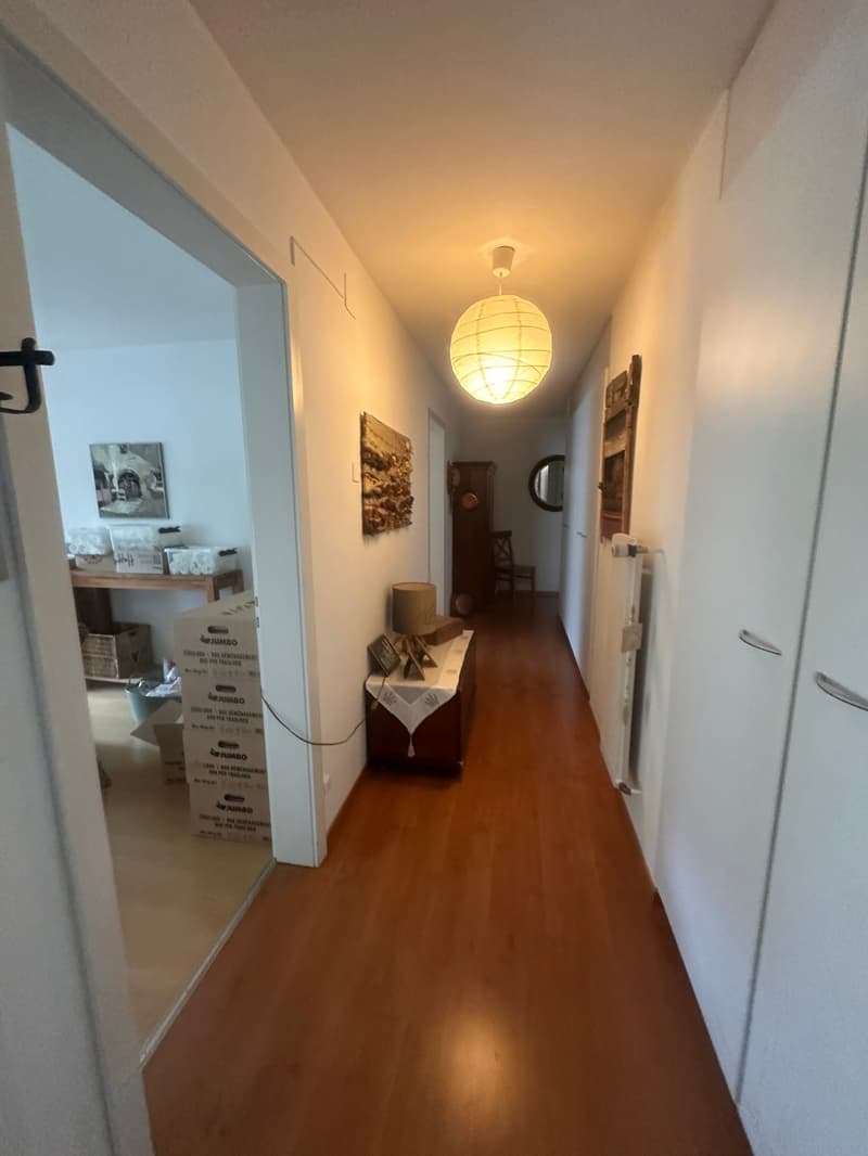 long hallway with wooden floor, white walls, boxes, lamp, mirror, radiator