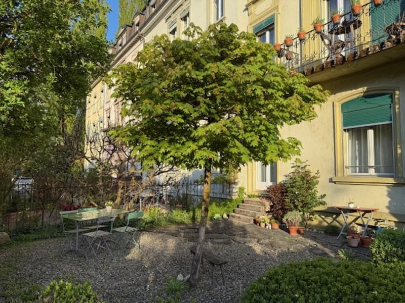 A garden with a table and chairs, a tree, plants, and a building with a balcony and windows