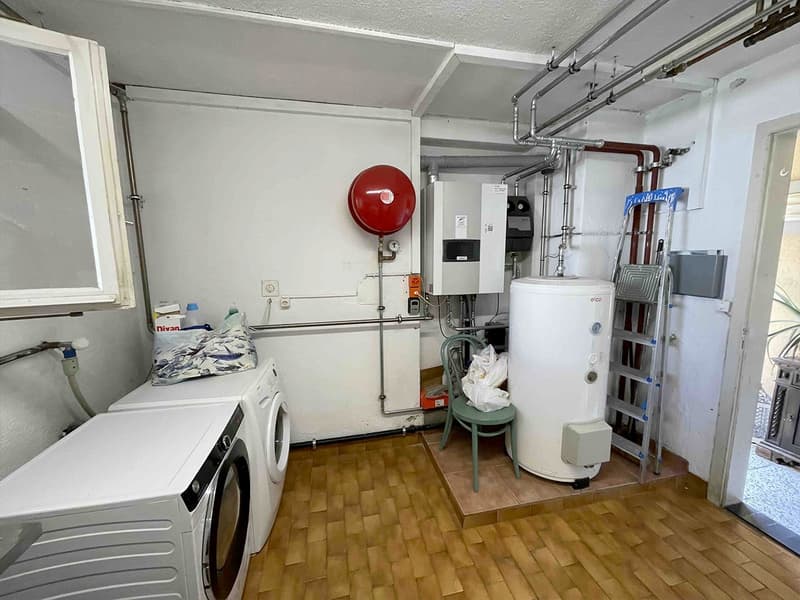 Wooden floor, white walls, laundry machines, green chair, white water heater, silver ladder