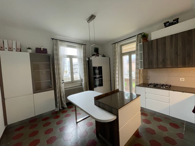 White kitchen with red hexagonal floor tiles, modern cabinets, an island with a kitchen counter and drawers, gas stove, and a table.